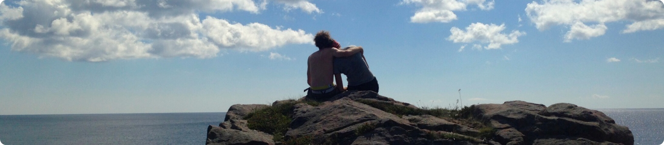 Two people sitting on a rock overlooking the ocean