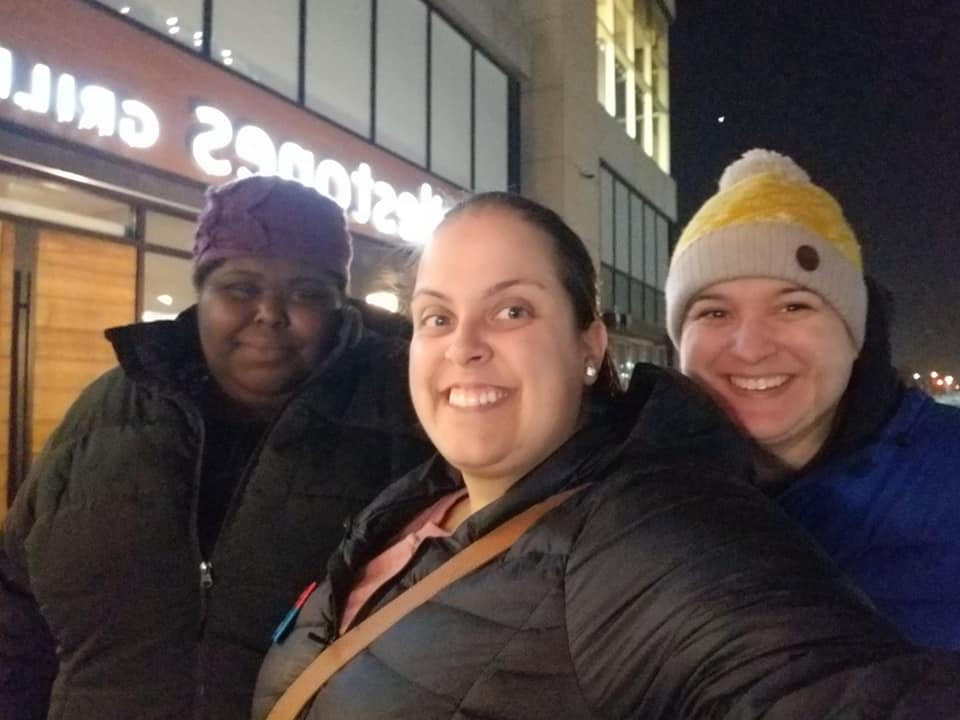 Charlene and two of her YACCer friends smile for a selfie outdoors on a cold evening. They are wearing hats and winter jackets.